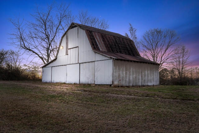 outdoor structure at dusk featuring an outbuilding, a yard, and a barn