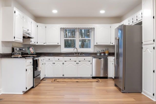 kitchen featuring dark countertops, appliances with stainless steel finishes, a sink, light wood-type flooring, and under cabinet range hood