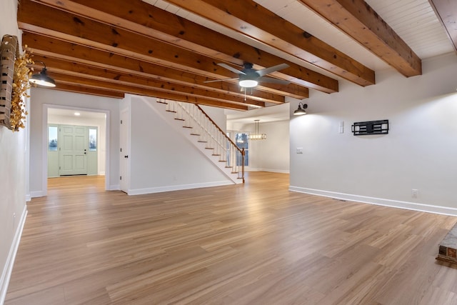 unfurnished living room with beamed ceiling, light wood-style floors, stairway, and baseboards