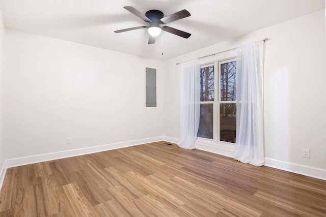 empty room with electric panel, ceiling fan, light wood-style flooring, and baseboards