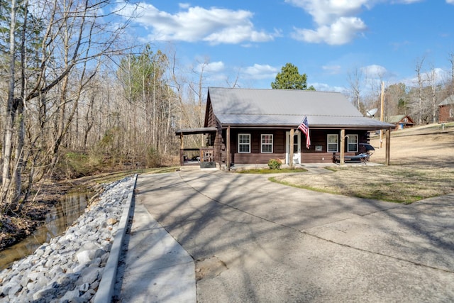 view of front of home with metal roof, an attached carport, covered porch, concrete driveway, and a front yard