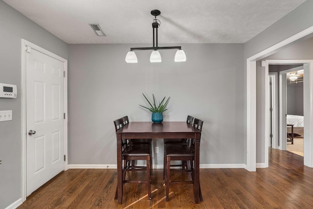 dining area featuring a textured ceiling, wood finished floors, visible vents, and baseboards