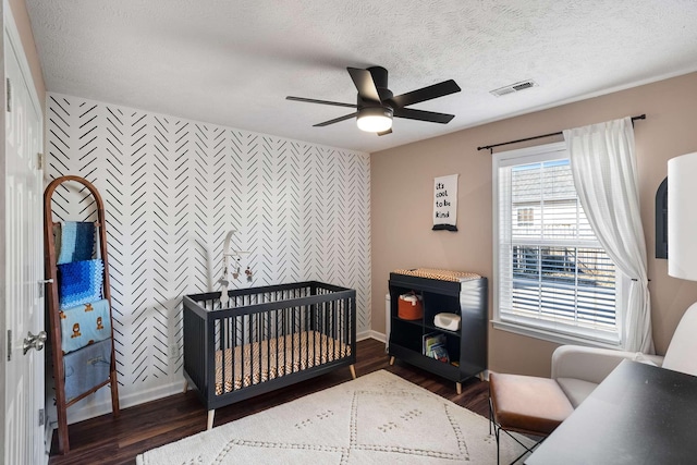 bedroom with a textured ceiling, an accent wall, wood finished floors, and visible vents