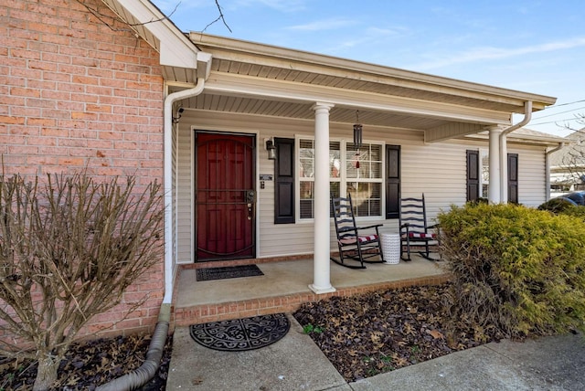 doorway to property featuring covered porch and brick siding