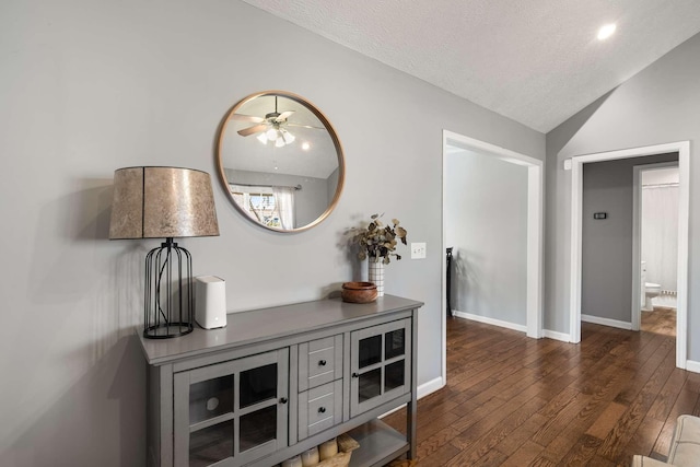 hall featuring vaulted ceiling, dark wood-style flooring, a textured ceiling, and baseboards