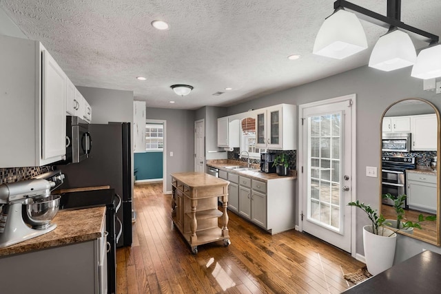 kitchen featuring dark wood-style floors, decorative backsplash, appliances with stainless steel finishes, white cabinetry, and a sink