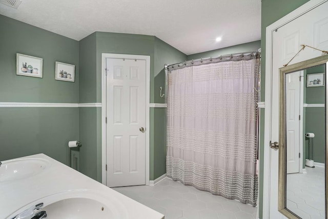 bathroom featuring a textured ceiling, double vanity, a shower with shower curtain, and a sink