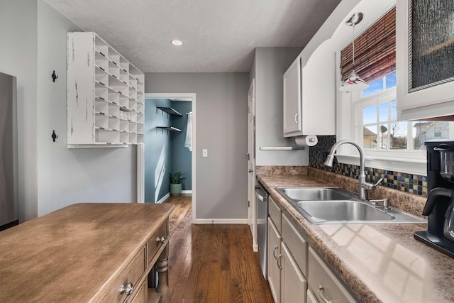 kitchen featuring dark wood-style flooring, a sink, baseboards, dishwasher, and tasteful backsplash