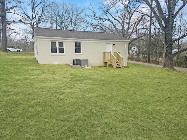 rear view of property with crawl space, roof with shingles, a lawn, and brick siding