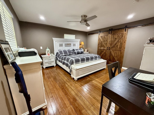 bedroom featuring a barn door, hardwood / wood-style floors, and a ceiling fan