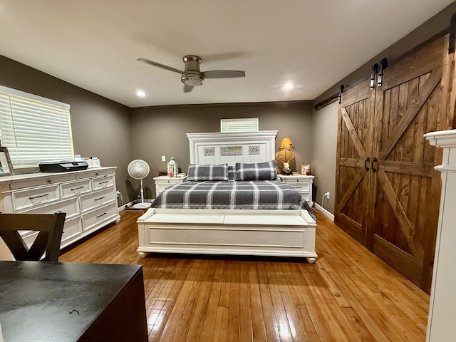 bedroom with a barn door, baseboards, ceiling fan, and hardwood / wood-style floors