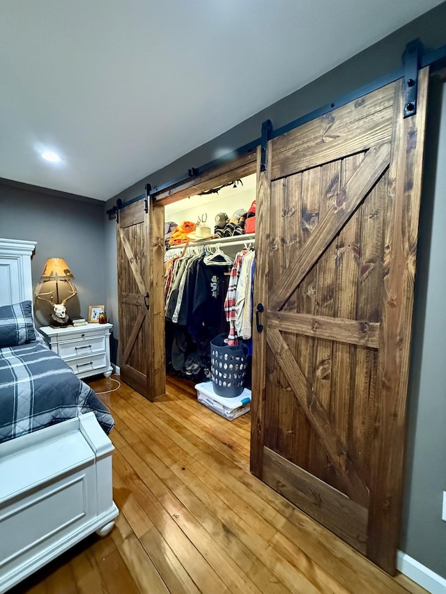 bedroom with a barn door, a closet, wood-type flooring, and baseboards