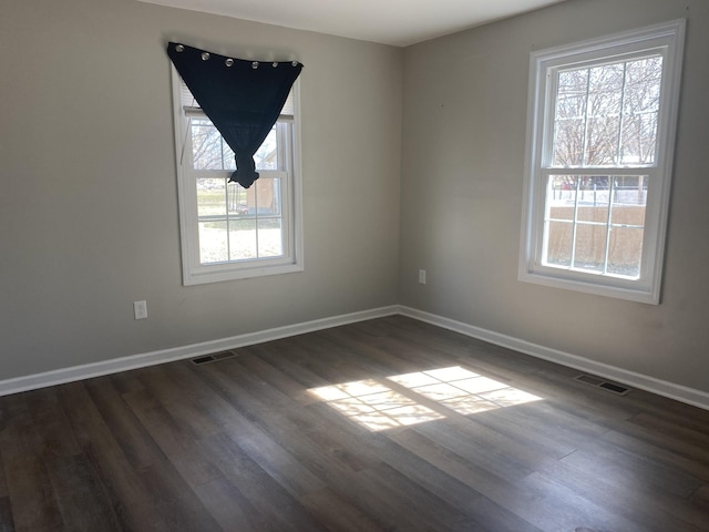 spare room with dark wood-type flooring, visible vents, and baseboards