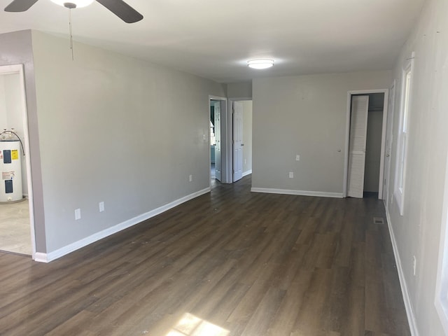 unfurnished room with a ceiling fan, water heater, baseboards, and dark wood-type flooring