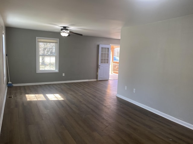 empty room featuring a ceiling fan, visible vents, baseboards, and dark wood-type flooring