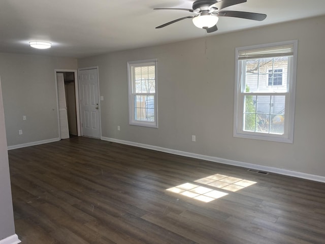 spare room featuring a ceiling fan, dark wood-style flooring, visible vents, and baseboards