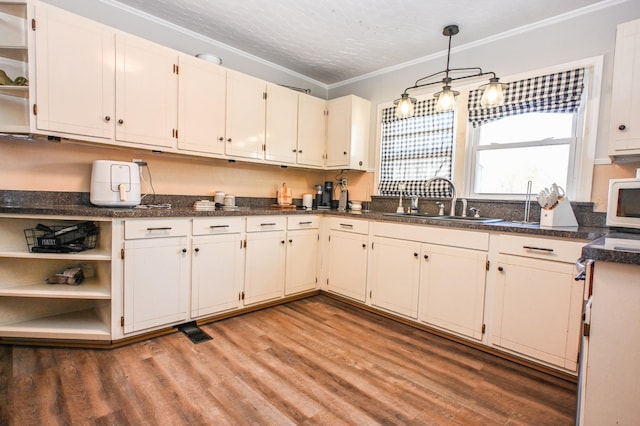 kitchen with white microwave, light wood-style flooring, a sink, ornamental molding, and pendant lighting