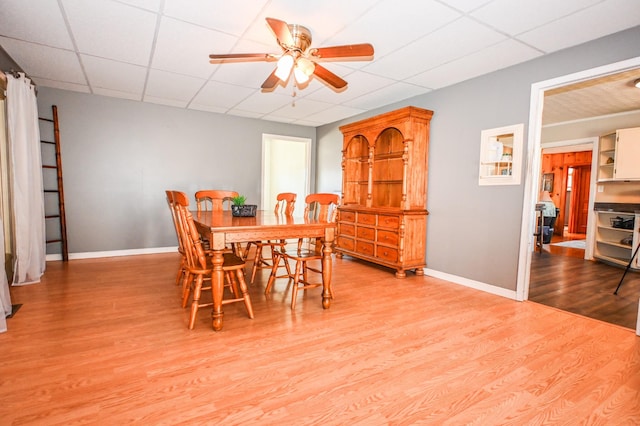 dining space featuring ceiling fan, baseboards, a drop ceiling, and wood finished floors