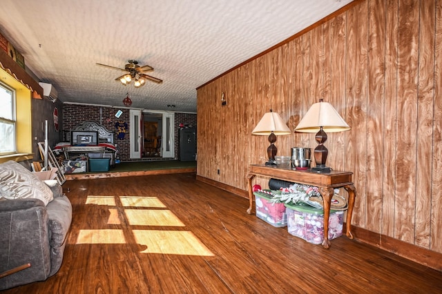 living room with wooden walls, a ceiling fan, wood finished floors, and a wall mounted air conditioner