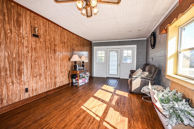 living area featuring concrete block wall, ceiling fan, baseboards, and wood finished floors