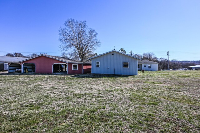 back of house with a yard, a detached garage, a carport, a pole building, and an outdoor structure