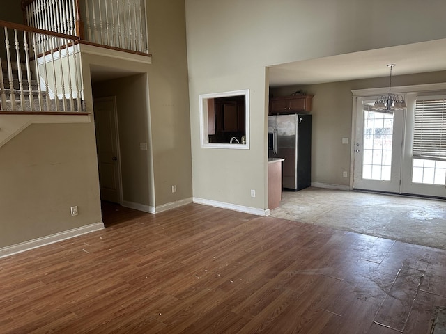 unfurnished living room with a notable chandelier, a high ceiling, wood finished floors, baseboards, and stairway