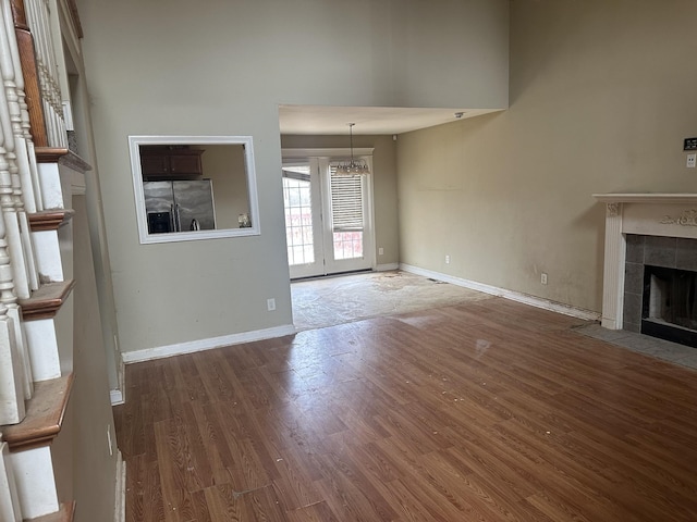 unfurnished living room with a chandelier, wood finished floors, a towering ceiling, baseboards, and a tiled fireplace