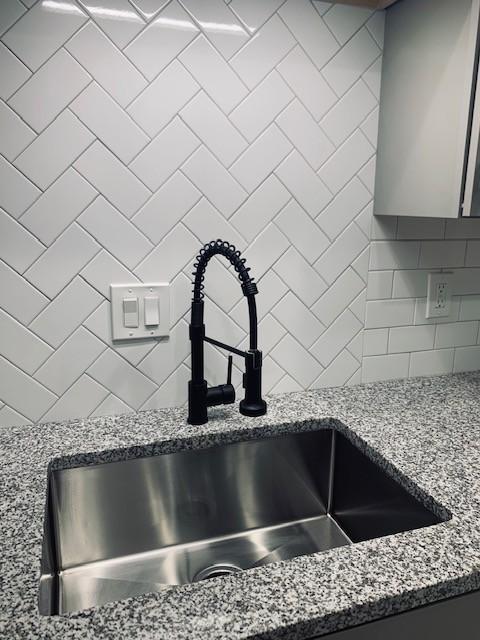 details featuring light stone counters, decorative backsplash, and a sink