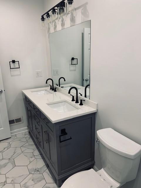 bathroom with toilet, marble finish floor, a sink, and visible vents