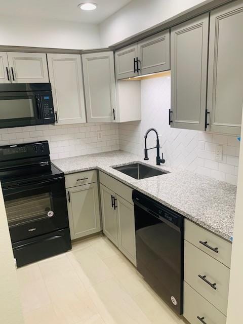 kitchen with light stone countertops, black appliances, decorative backsplash, and a sink