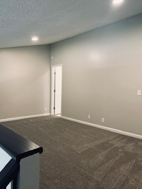 empty room with baseboards, dark colored carpet, and a textured ceiling