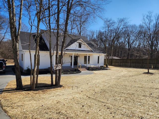 modern inspired farmhouse featuring covered porch, roof with shingles, and fence