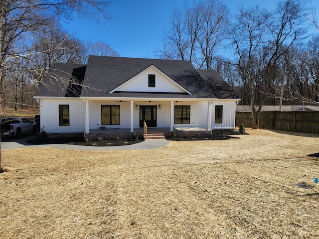 modern farmhouse with a porch, a shingled roof, and fence