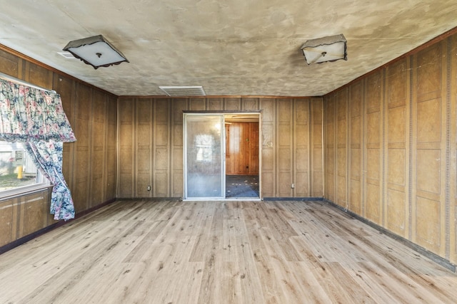 spare room with wooden walls, visible vents, and light wood-style flooring