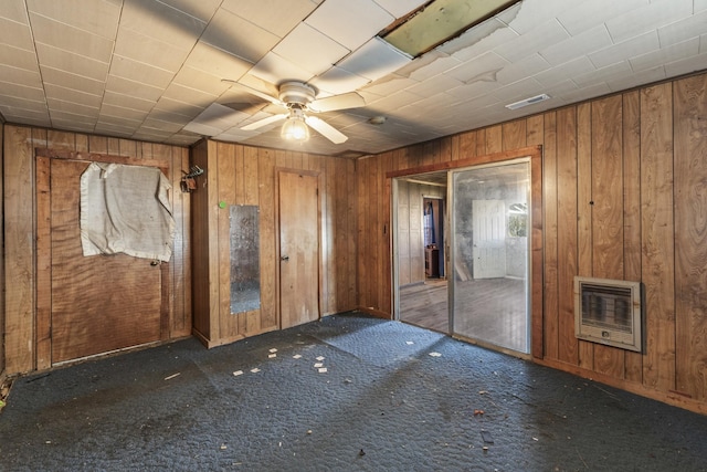 empty room with ceiling fan, wooden walls, carpet floors, visible vents, and heating unit