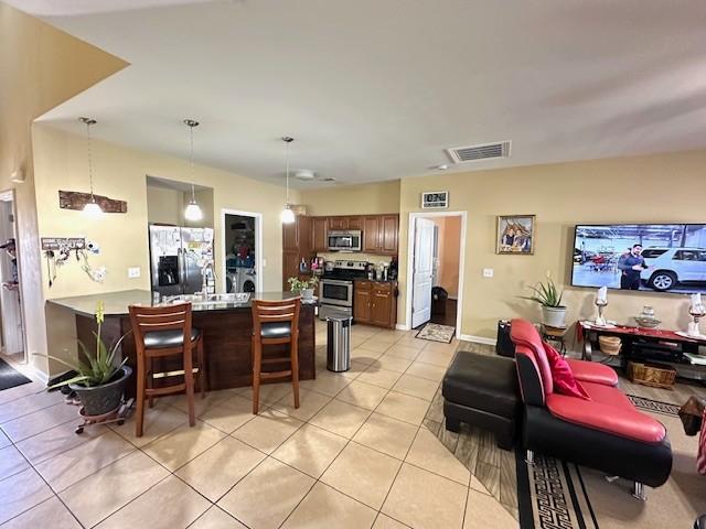 interior space featuring light tile patterned floors, visible vents, appliances with stainless steel finishes, a breakfast bar area, and a peninsula