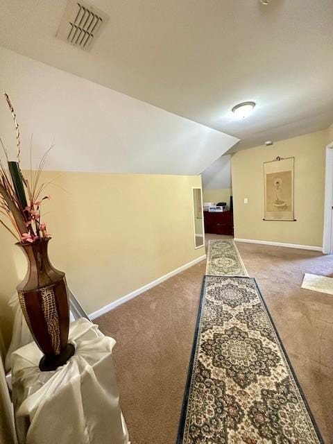 corridor with carpet floors, lofted ceiling, visible vents, and baseboards