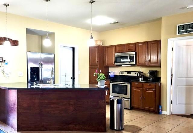 kitchen with light tile patterned flooring, stainless steel appliances, visible vents, hanging light fixtures, and dark countertops