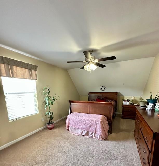 bedroom with a ceiling fan, light carpet, vaulted ceiling, and baseboards