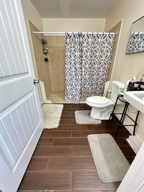 full bathroom featuring toilet, a tile shower, and wood finish floors