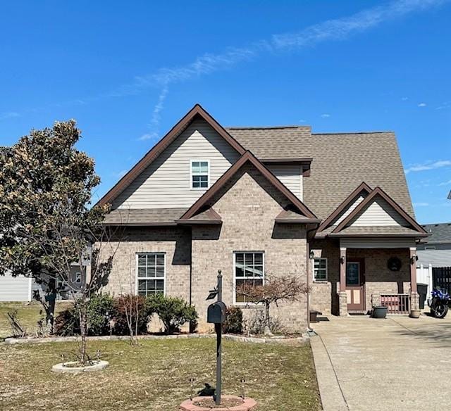 view of front of property featuring brick siding, a front lawn, and roof with shingles