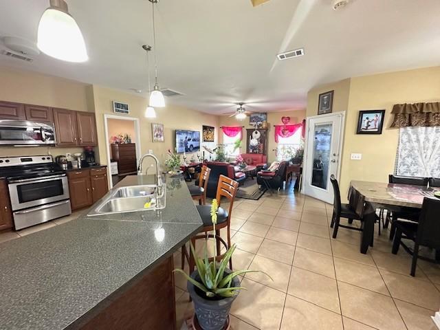 kitchen with a breakfast bar area, stainless steel appliances, a sink, visible vents, and dark countertops
