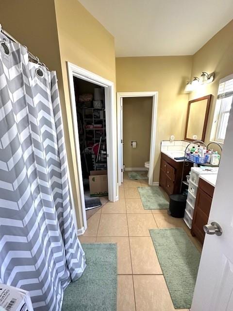 bathroom featuring curtained shower, toilet, vanity, baseboards, and tile patterned floors