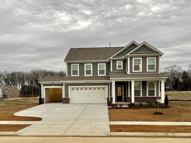 craftsman-style house featuring roof with shingles, a porch, concrete driveway, and brick siding