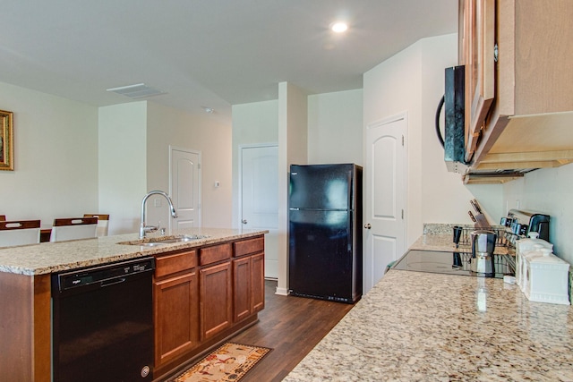 kitchen featuring dark wood finished floors, brown cabinetry, a kitchen island with sink, a sink, and black appliances