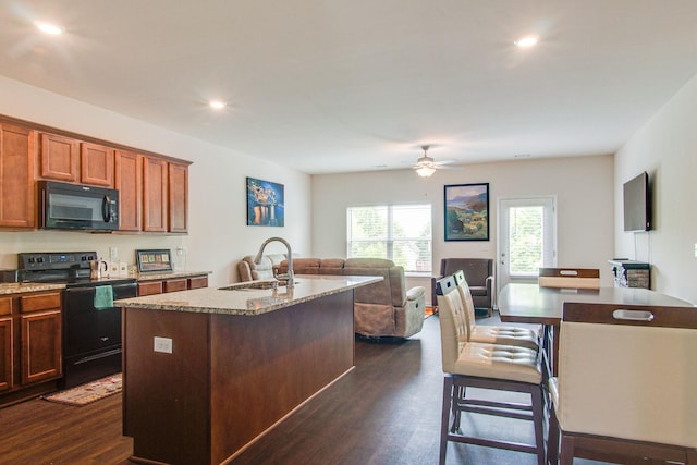 kitchen with black appliances, dark wood-type flooring, an island with sink, and a sink