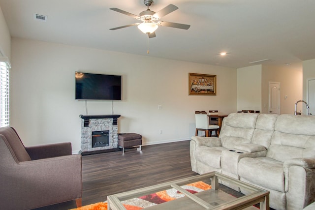 living area featuring dark wood-style flooring, a fireplace, visible vents, a ceiling fan, and baseboards