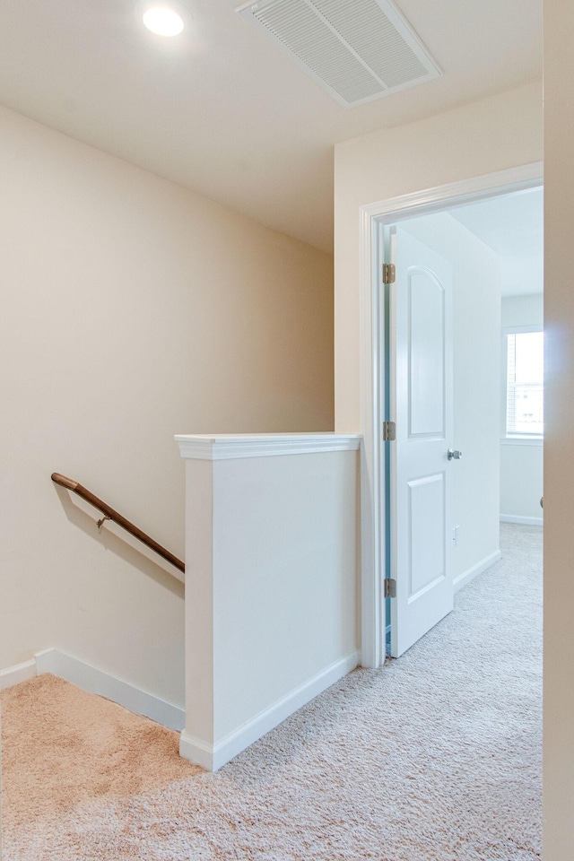 hall with carpet floors, an upstairs landing, visible vents, and baseboards