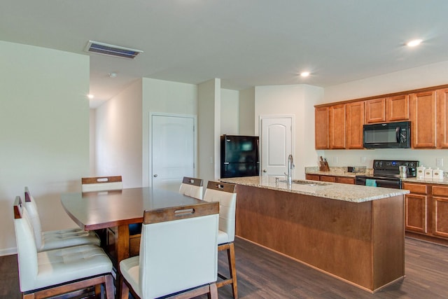 kitchen with visible vents, dark wood-type flooring, a sink, an island with sink, and black appliances