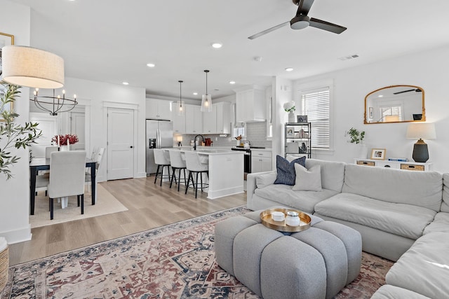 living area with recessed lighting, visible vents, light wood finished floors, and ceiling fan with notable chandelier